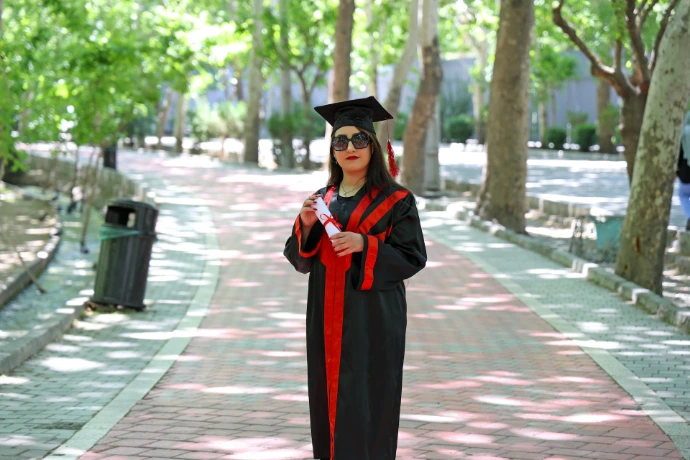 A woman in graduation gown and cap stands outside